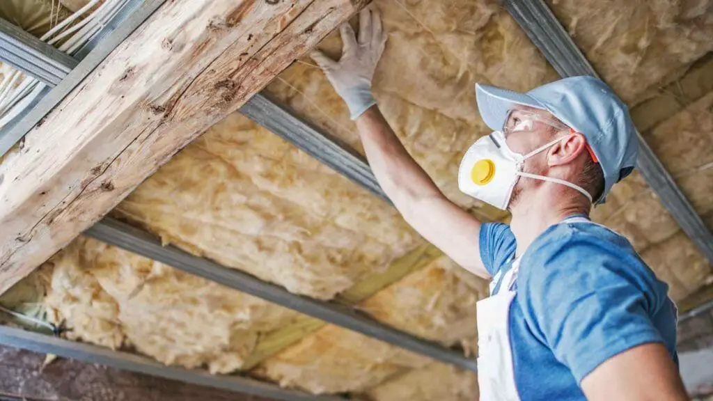 Photo of a person applying rock wool insulation to the ceiling of a sunroom.