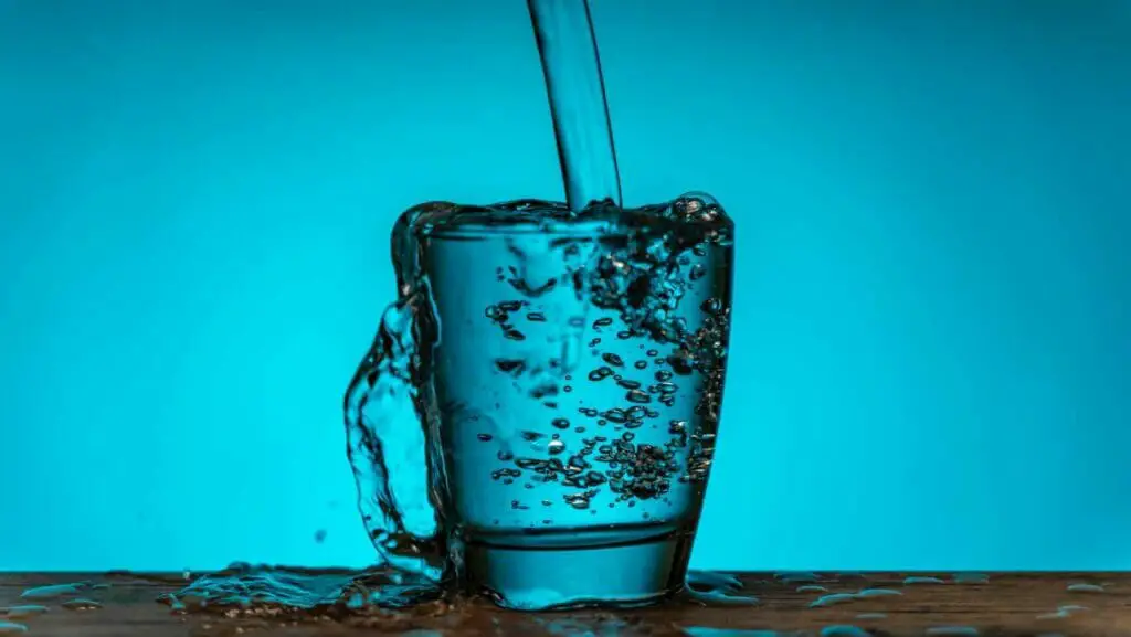 Photo of a up being filled with water a blue background and the table full of water.