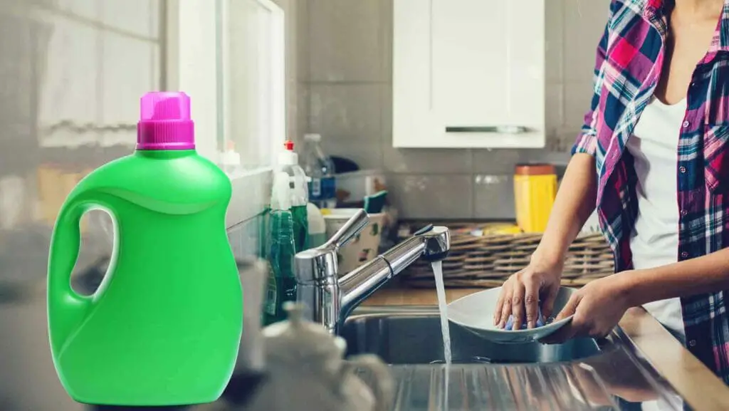 Photo of a woman washing dishes by hand with laundry detergent by its side. Can You Use Laundry Detergent to Wash Dishes?