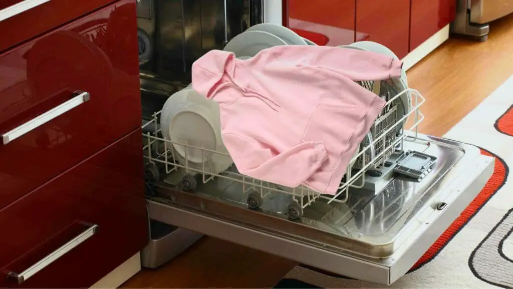 Photo of an open dishwasher and a hoodie on top of the dishes on the dishwasher. Can You Wash Clothes in a Dishwasher?